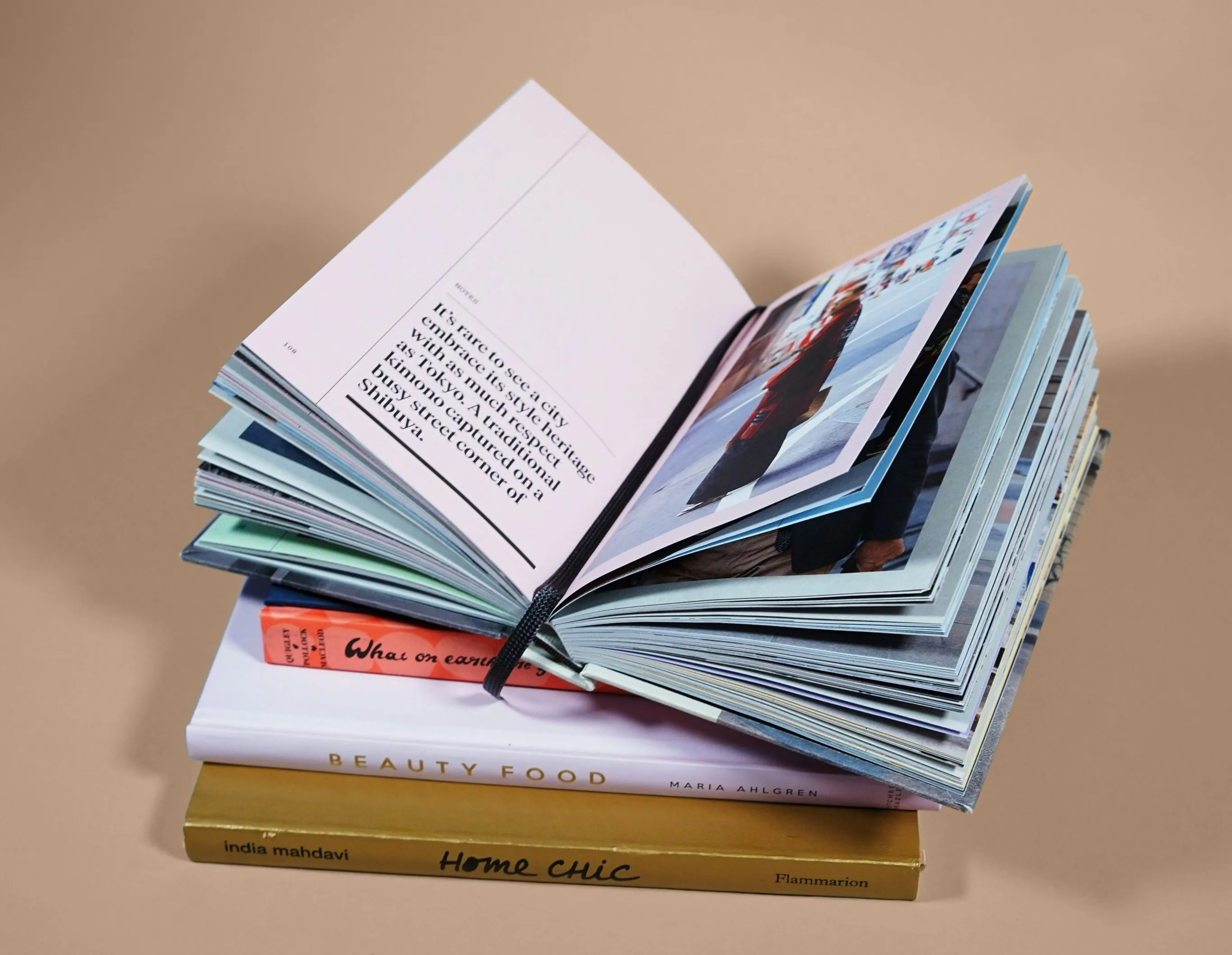 Foto buku terbuka di atas tumpukan buku pada latar krem.